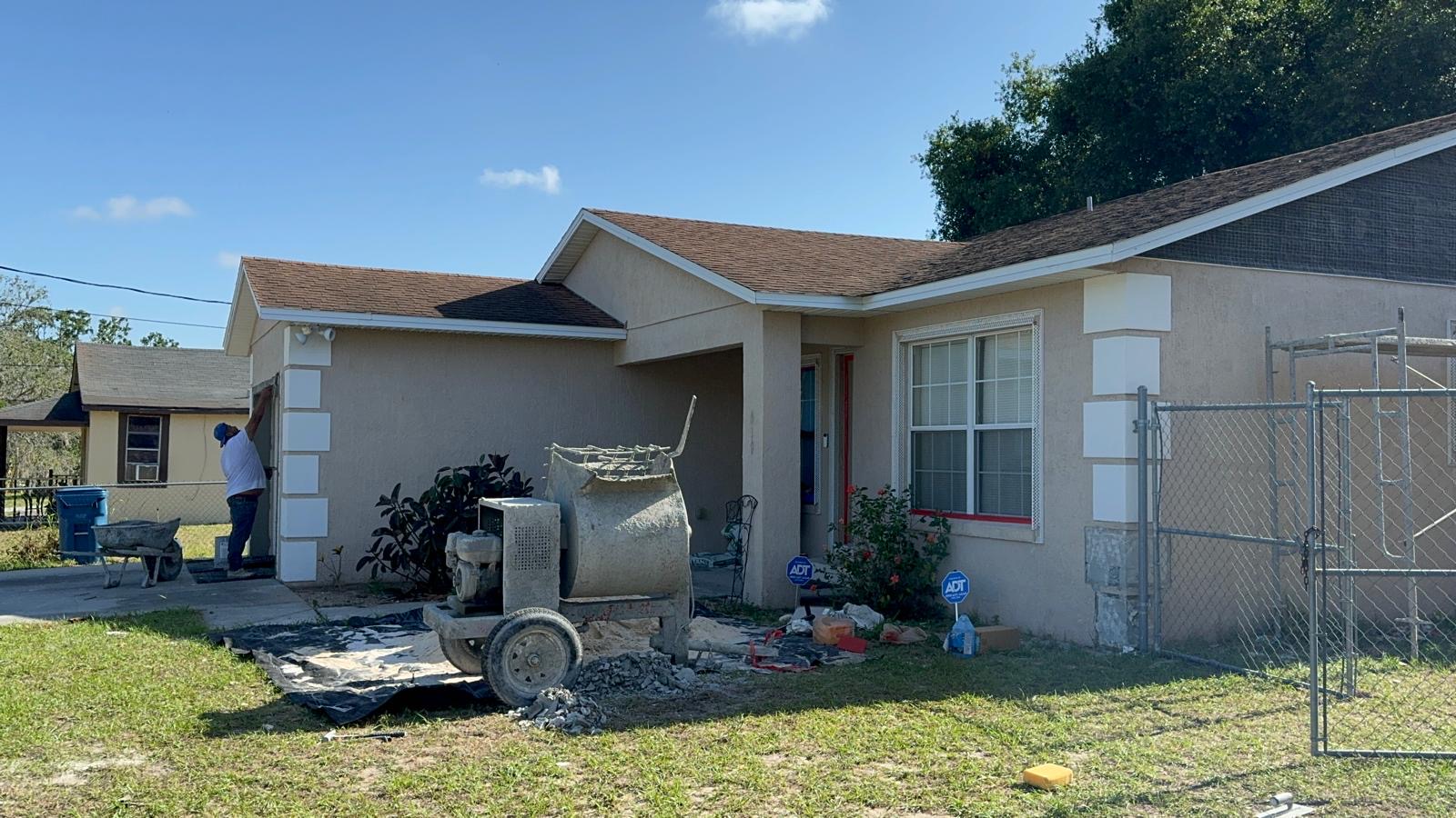 Crew resurfacing exterior stucco walls with a mixer set up in the front yard