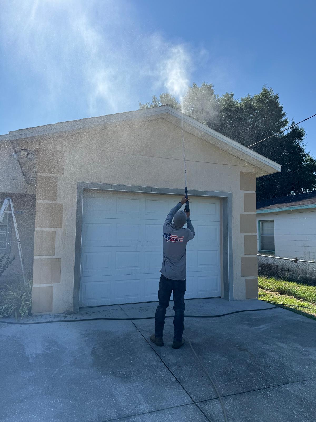 Worker pressure washing the gable and garage exterior of a house