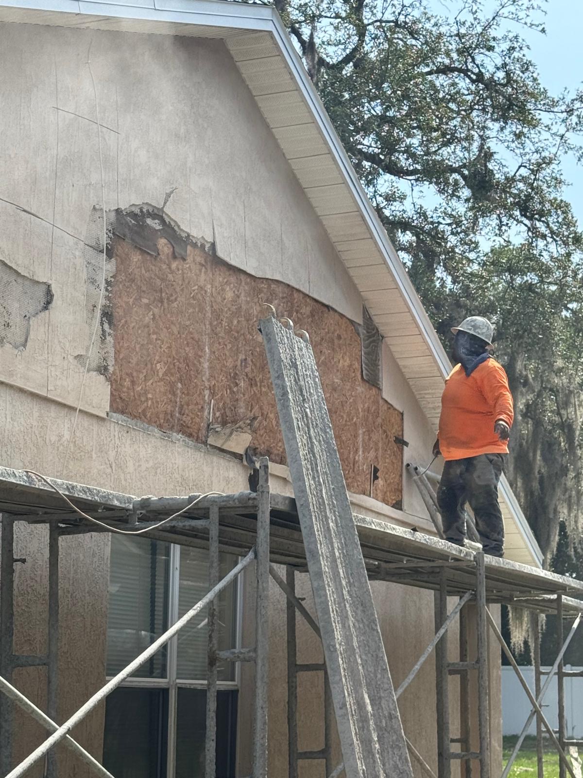 Worker on scaffolding repairing damaged stucco on a home gable