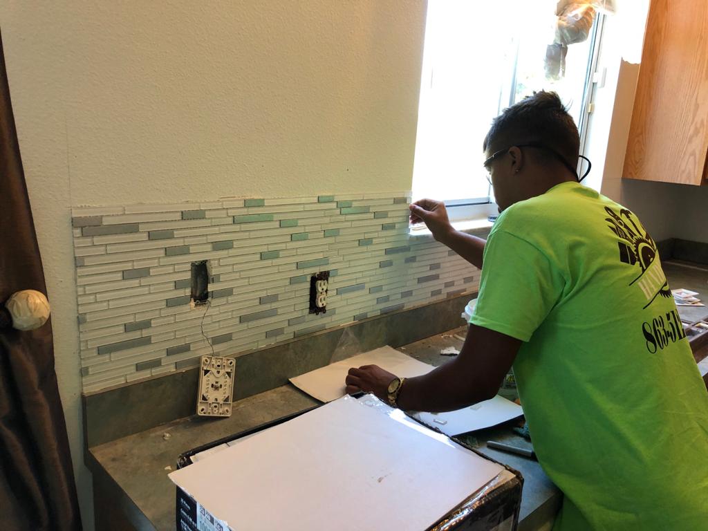Technician setting glass mosaic backsplash tiles on a kitchen wall