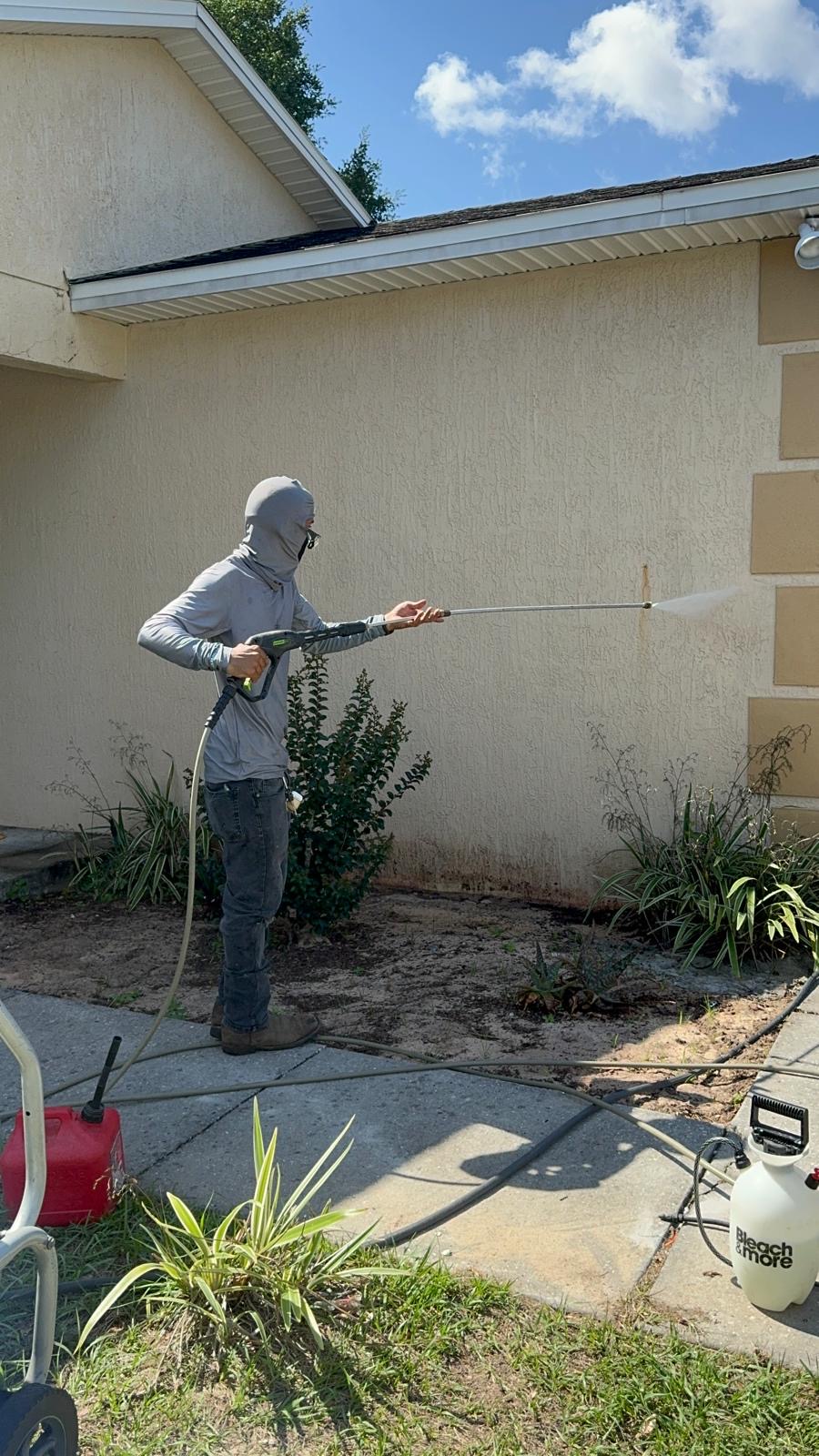 Technician soft washing stained exterior stucco walls with a pressure washer