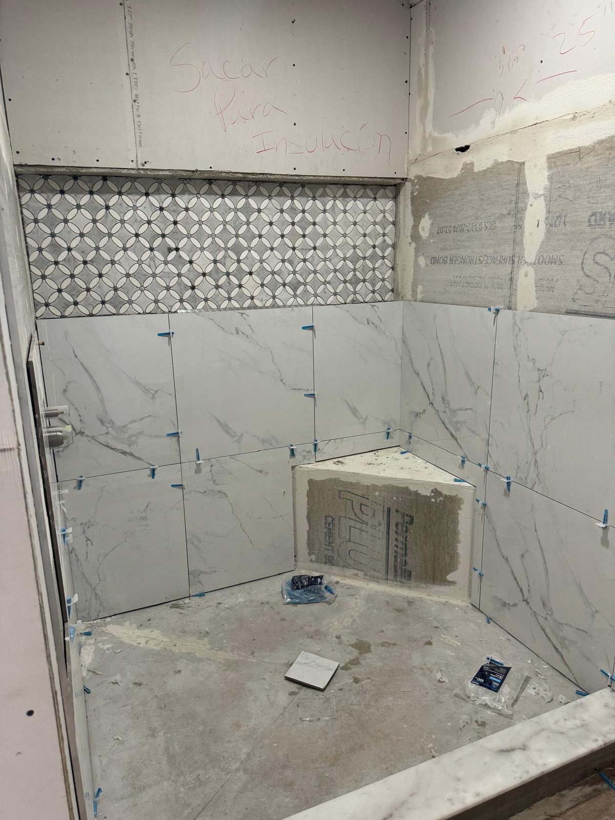 Large-format marble-look tile installed on shower walls with a patterned mosaic niche