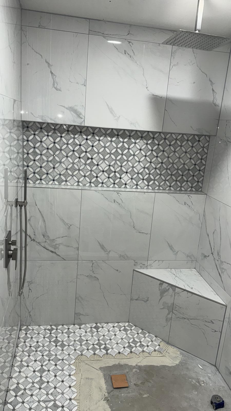 Finished marble-tile walk-in shower with corner bench, rainfall head and mosaic accent band
