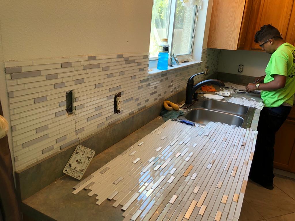 Glass mosaic backsplash tile being installed along a kitchen counter and sink wall