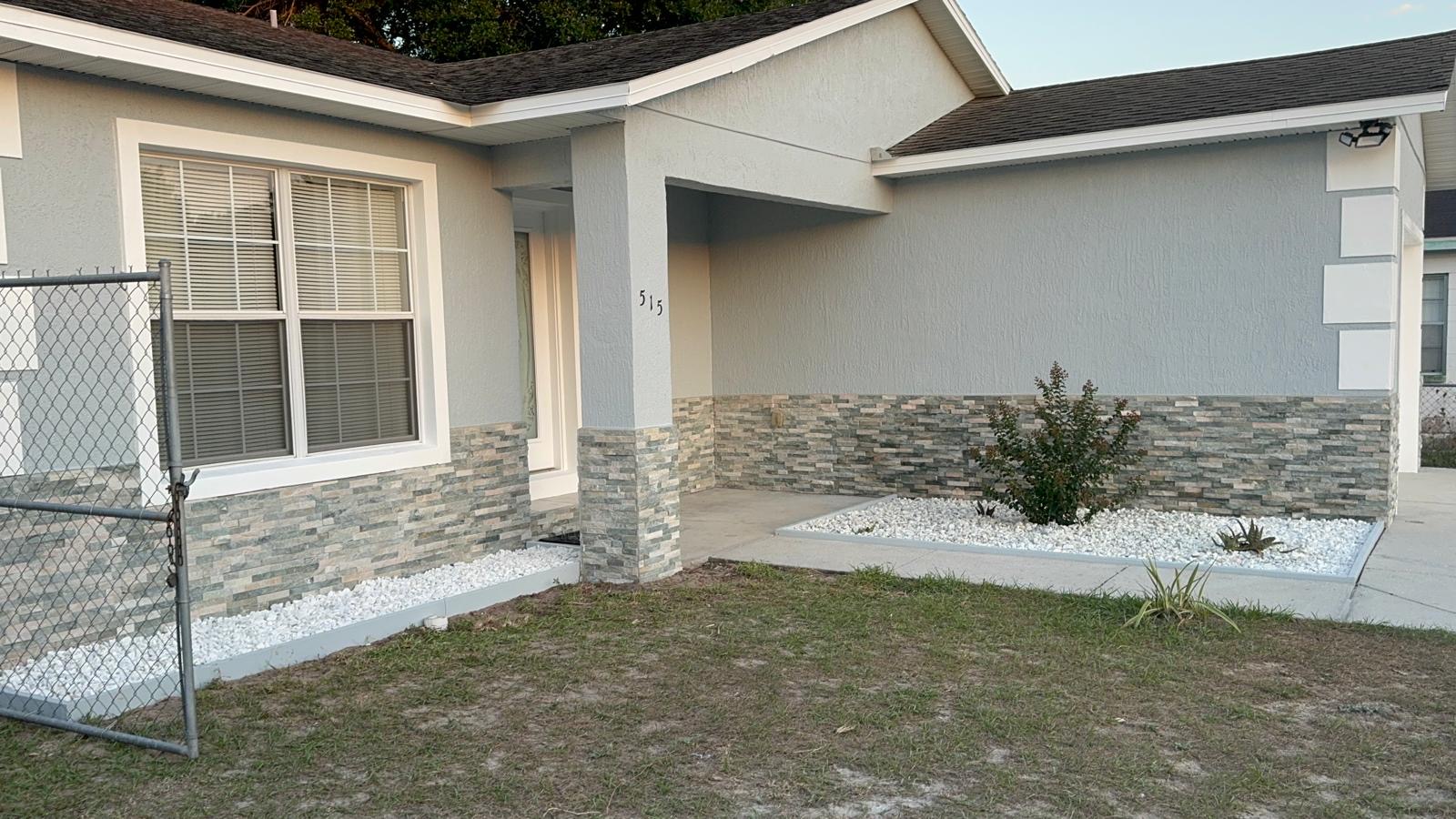 Completed exterior paint job with stone accent wall and white rock landscaping bed